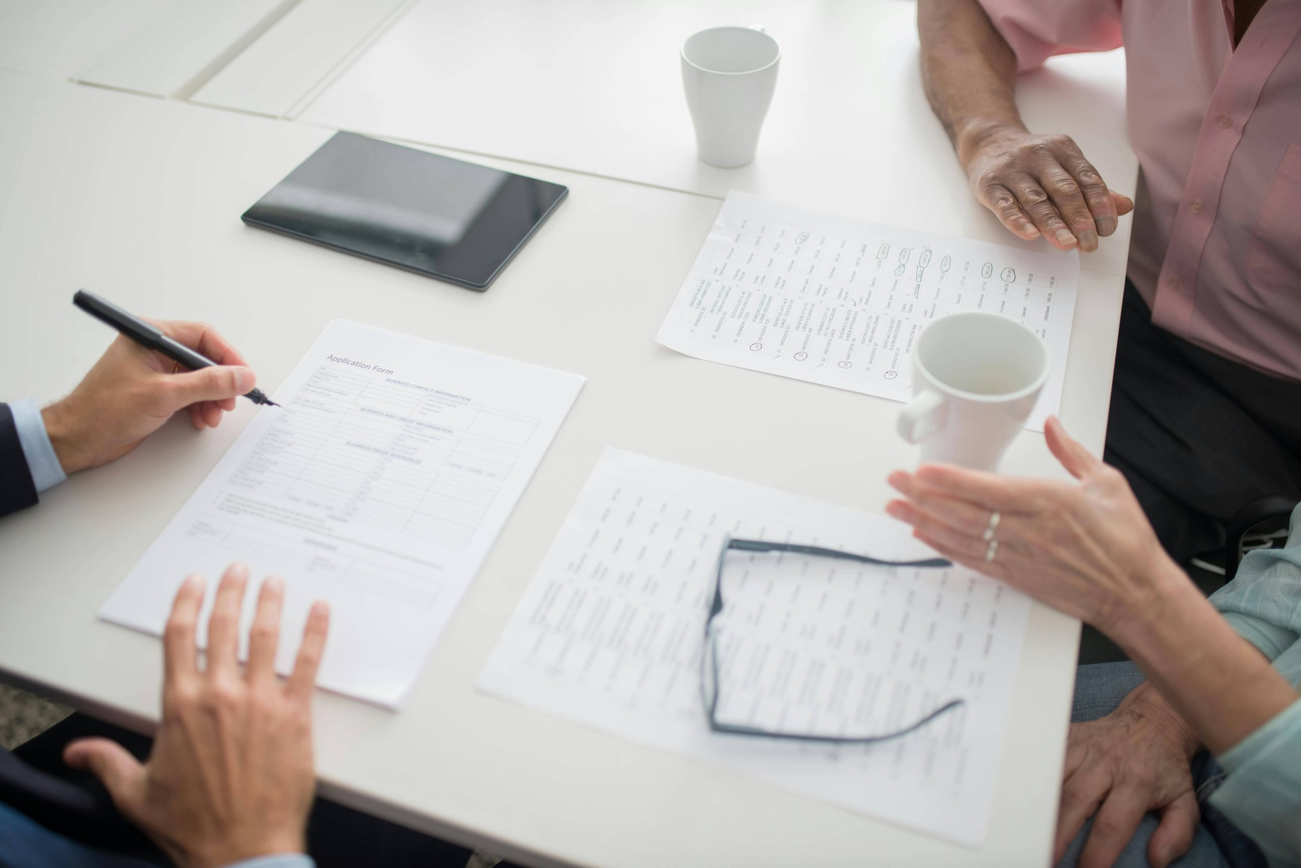 Équipe de professionnels travaillant ensemble autour d'une table avec documents, tablette et café lors d'une réunion de travail